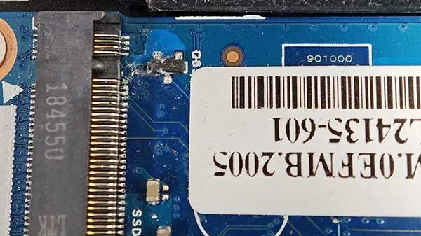 Placa base de portátil con corrosión y daños por humedad en la zona del conector SSD.